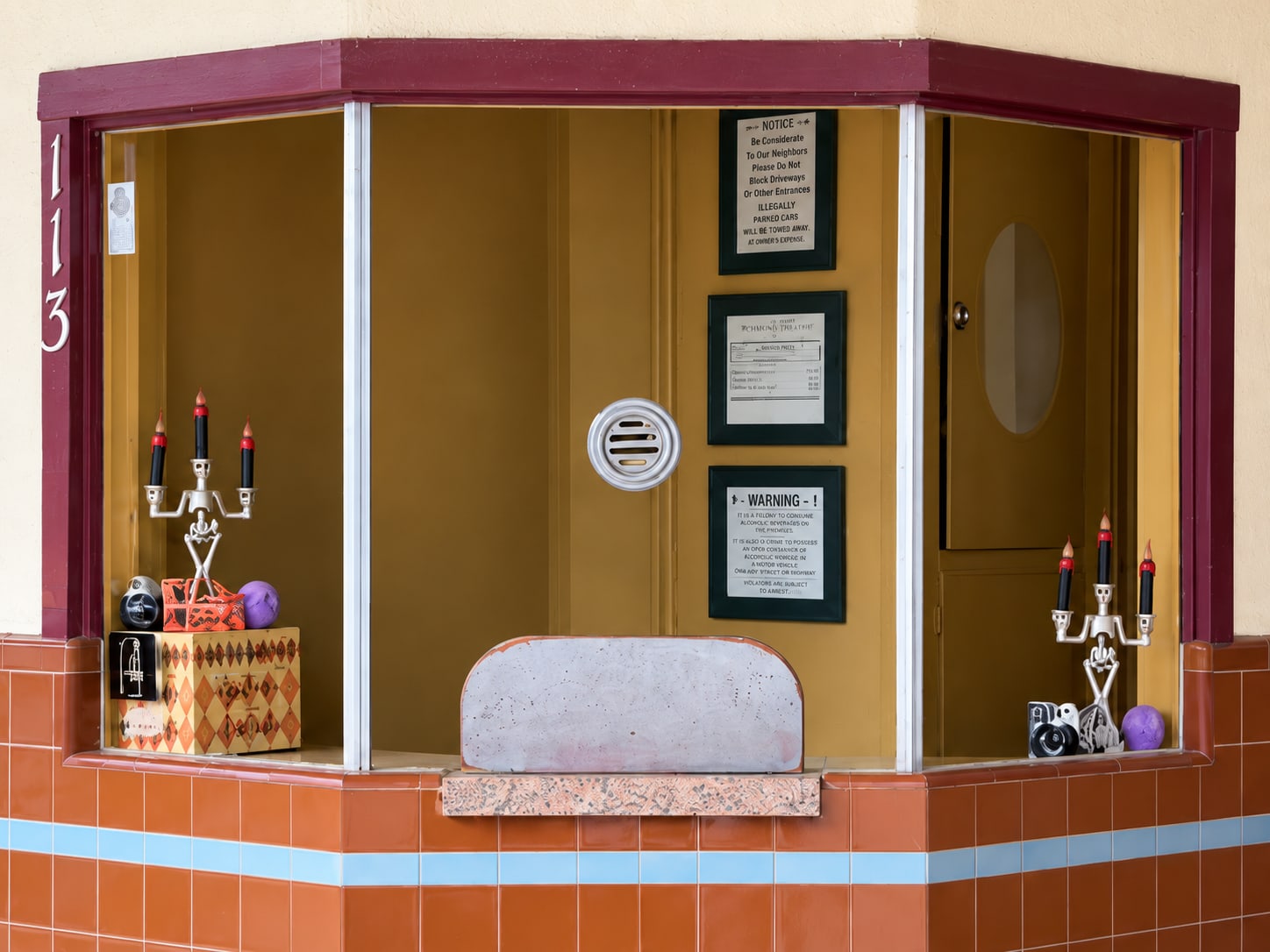 The LanTex box office window at 113 W Main St: a maroon frame over orange and blue tile, the round speaking grille and posted notices behind the glass