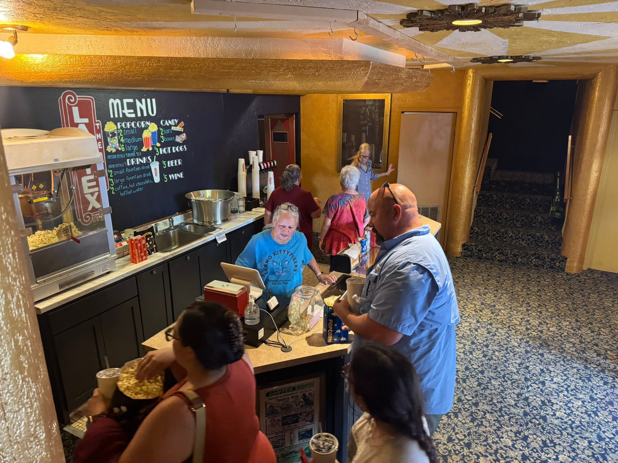 A volunteer working the LanTex concession stand, the chalkboard menu and popcorn machine behind her, moviegoers lined up at the counter